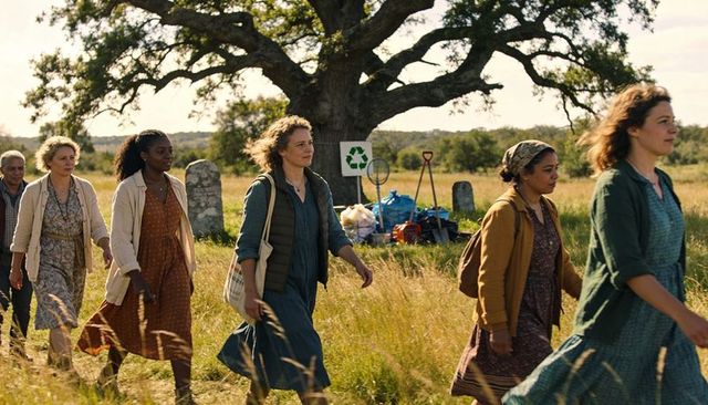 Volunteers walking through rural cemetery by oak tree carrying recycling bags and tools