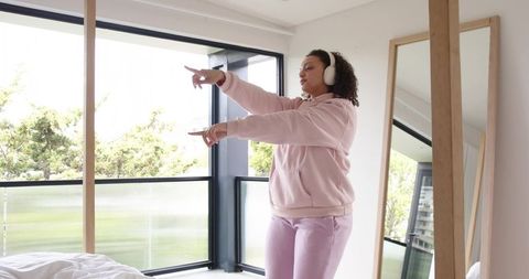 African american woman dancing and pointing by balcony wearing pink hoodie and headphones
