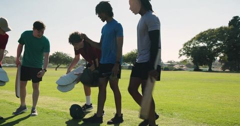 Young diverse male teammates carrying bats and gear across sunlit field sharing camaraderie