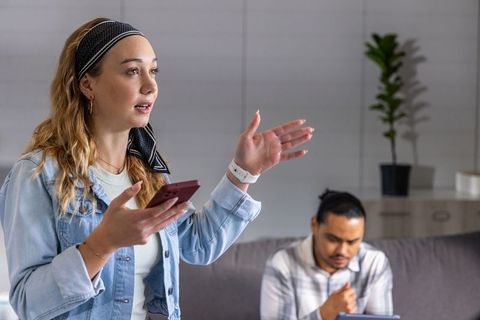 Young woman presenting with smartphone while colleague using tablet in office lounge