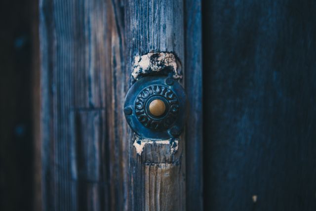 This image displays an old, weathered doorbell mounted on an aged wooden door. Ideal for use in articles about vintage architecture, historical buildings, or rustic design. Great for illustrating concepts related to decay, age, or antiquity.