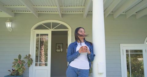 Morning coffee on porch: woman leaning on column holding mug in casual denim
