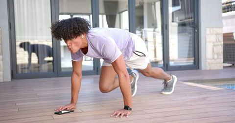 Young Man Exercising with Smartphone Outdoors on Wooden Deck
