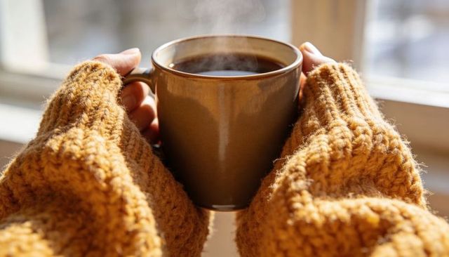 Cozy hands cradling steaming coffee mug wearing chunky mustard knit sleeves, morning calm