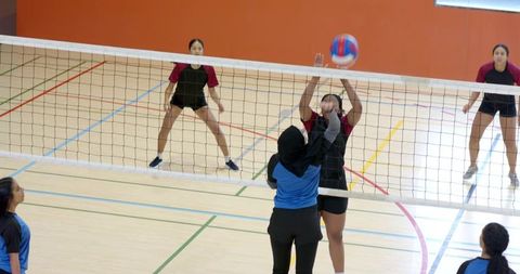 Indian athlete in headscarf blocking volleyball at indoor court during team match