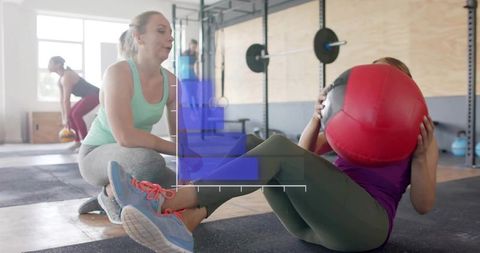 Female trainer spotting client doing medicine ball sit-up during functional fitness class