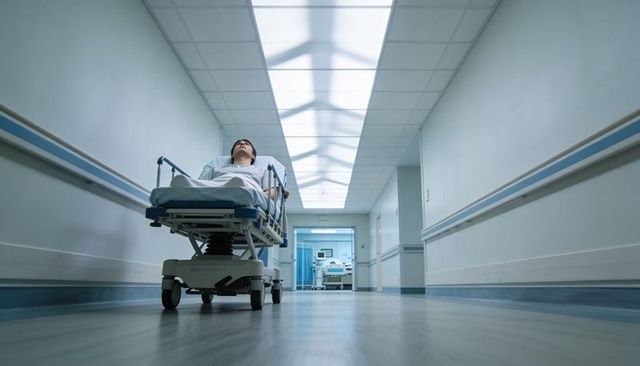 Adult male patient lying on stretcher in sterile hospital corridor under fluorescent lights