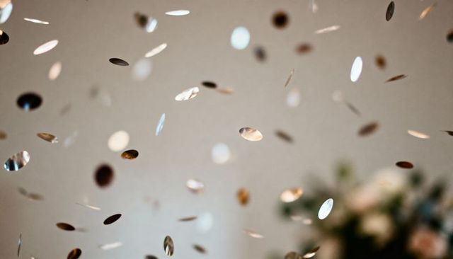 Metallic confetti discs floating against beige background with soft bokeh and foliage