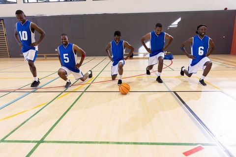 African american basketball team warming up with lunges on indoor hardwood court