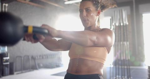 Woman swinging kettlebell in industrial gym during intense strength training