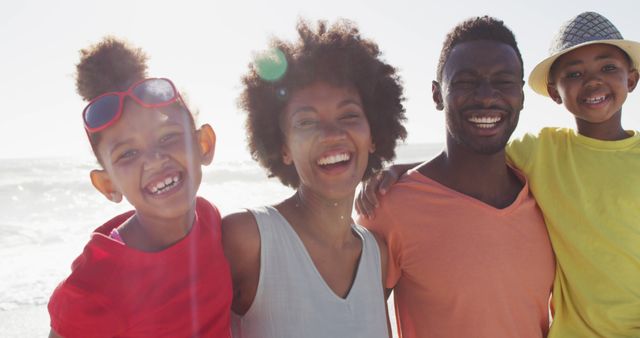 African American family of four enjoying a sunny day at the beach. Great for depicting family bonding, summer vacations, outdoor fun, and happy moments. Ideal for advertisements, travel agencies, promotional material, and articles about family life, leisure activities, or tourism.