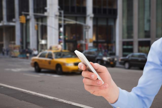 This image shows a close-up view of a hand holding a smartphone against the background of a busy city street with a yellow taxi in motion. Ideal for illustrating themes related to urban life, mobile technology, transportation, and connectivity. Great for blogs, articles or advertisements about urban lifestyle, mobile apps, travel, or modern communication.