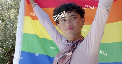 Young man raising rainbow flag in garden celebrating pride with joyful smile and vibrant colors