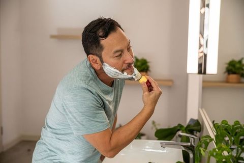 Mature asian man applying shaving cream with brush at modern bathroom vanity