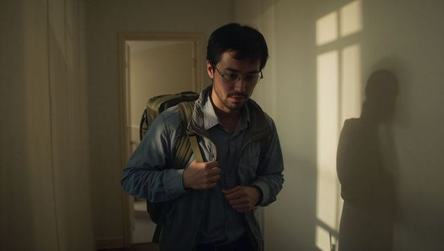 Young man adjusting backpack straps in dim hallway casting window light and shadow