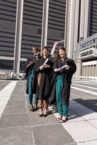 Rooftop graduation celebration: female graduates smiling, holding diplomas in city