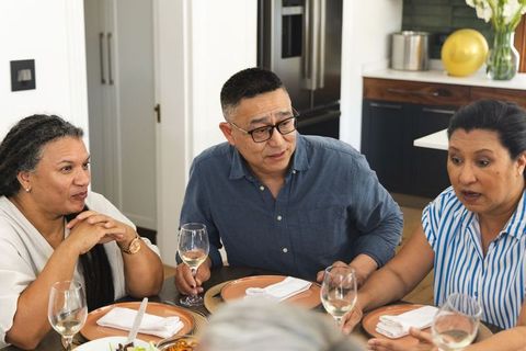 Diverse friends sharing warm dinner conversation around kitchen dining table with wine