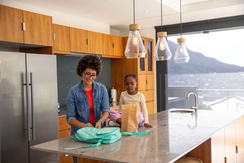 Mother and daughter packing backpack in modern kitchen