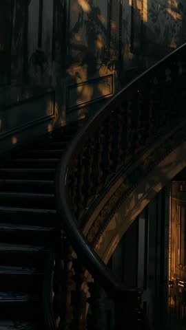 Vertical video panning down antique spiral staircase with golden light and dust motes