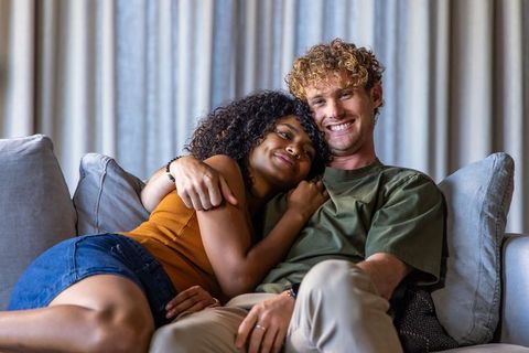 Young couple cuddling on sofa, sharing warm embrace and joyful smile while showing ring