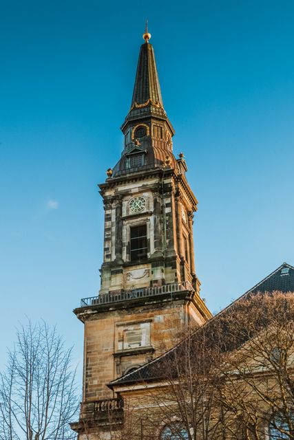 Tall church tower and steeple against clear blue sky. Ideal for illustrations of historic architecture, religious settings, travel destinations, and cultural landmarks. Perfect for use in brochures, articles, and graphics about Christianity, history, or architectural styles.