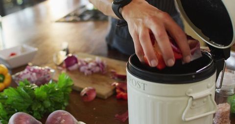 Person Composting Vegetable Peels During Meal Preparation