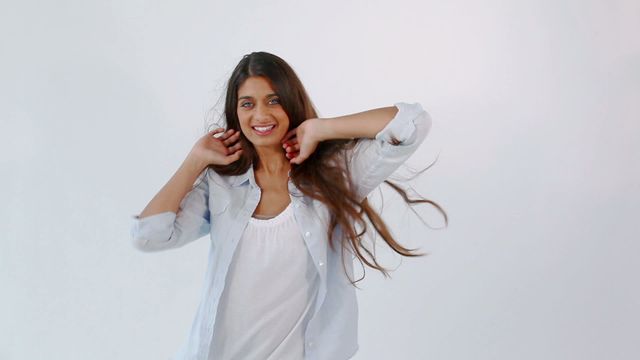 Young woman with long brown hair dancing joyfully in casual white outfit against a plain white background. Perfect for use in advertising, lifestyle blogs, fitness promotions, or any creative project needing a happy and carefree vibe.