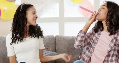 Women Laughing Together on Couch at Festive Indoor Party