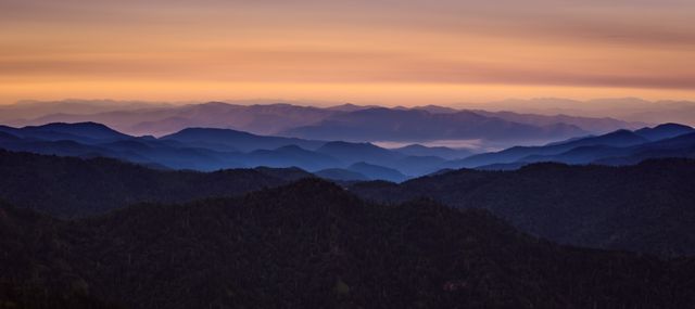 Peaceful sunrise overlooking layered mountain ranges with silhouettes of peaks stretching into the horizon. Ideal for use in travel brochures, nature calendar, background for presentations, or desktop wallpapers. Highlights the beauty of nature and the serenity of early morning landscapes.