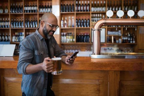 Man Enjoying Beer and Using Smartphone at Wooden Bar Counter