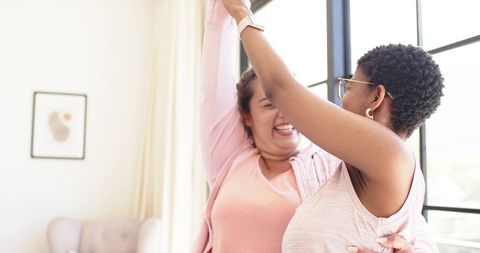 Laughing african american friends embracing and celebrating in sunlit cozy living room
