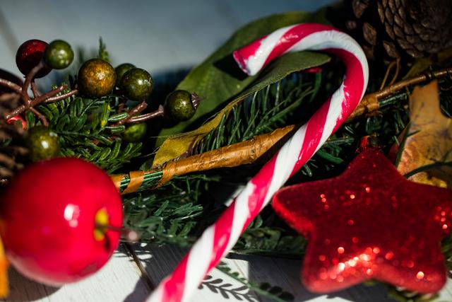 This image captures a close-up view of traditional Christmas decorations, including a candy cane, red glittery star, pine cones, and berries, arranged on a wooden plank. Ideal for use in holiday greeting cards, festive advertisements, social media posts, and seasonal blog articles.