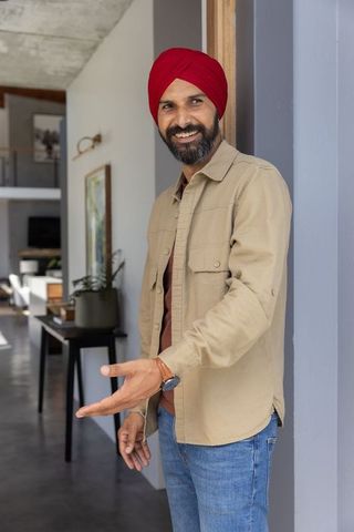 Smiling indian man welcoming guests at home entrance with open hand gesture
