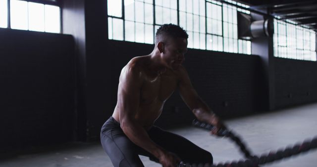 Shirtless african american man exercising battling ropes in an empty urban building. urban fitness and healthy lifestyle.