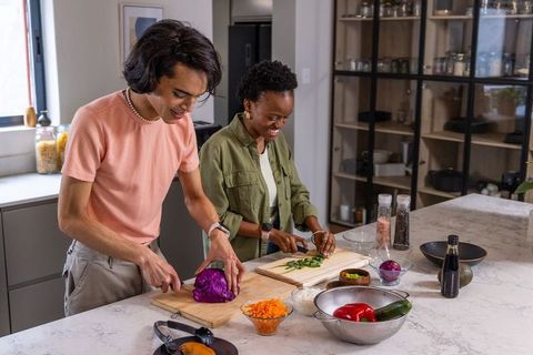 Diverse couple chopping colorful vegetables on marble kitchen island, preparing healthy meal