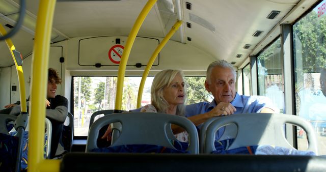 Senior couple sits near window, observing surroundings during bus ride, sign visible on wall. Ideal for themes of retirement, travel, and public transportation. Use in materials advocating for senior travel independence, public transport advertisements, or editorial content about urban commuting experiences.