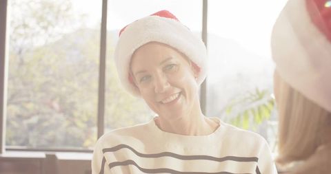 Sunlit friends wearing santa hats sharing warm holiday smile in cozy living room