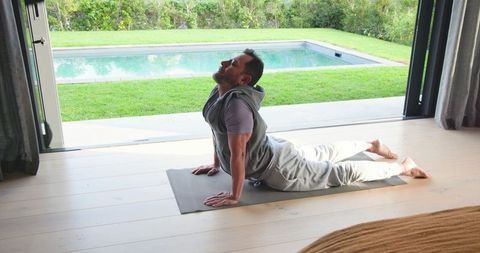 Man in Hoodie Practicing Backbend Yoga at Home Overlooking Pool