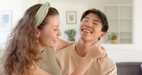 Diverse couple laughing and embracing on sofa in bright neutral living room