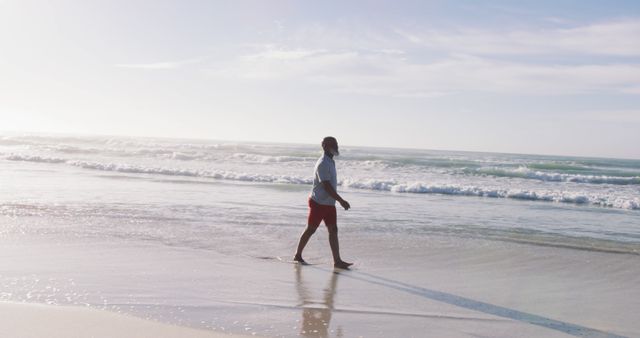 Senior african american man walking at the beach. healthy outdoor leisure time by the sea.
