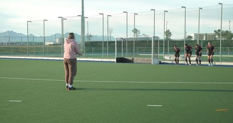 Female coach instructing teenage hockey team on field