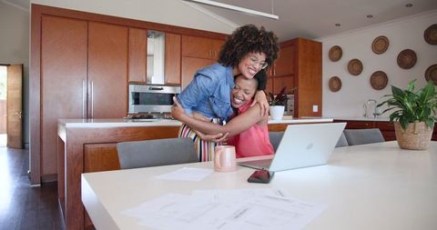 Diverse Female Couple Celebrating Success with Laptop in Modern Kitchen