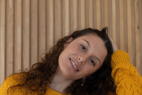 Smiling young woman tilting head wearing mustard sweater and hoop earrings warm portrait