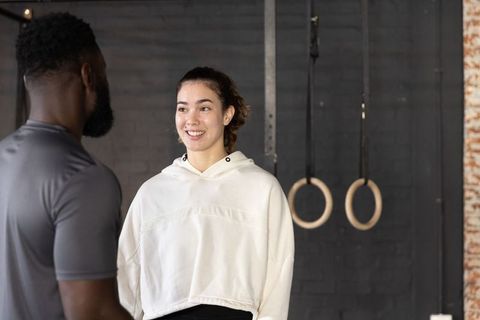 Female in cropped hoodie training with african american male trainer in industrial gym