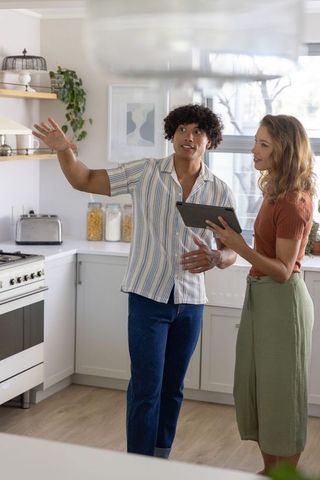 Couple discussing modern kitchen renovation holding tablet and gesturing toward oven