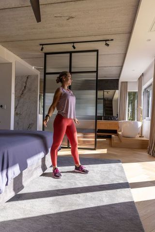 Woman stretching in sunlit minimalist master suite wearing workout gear and tracker