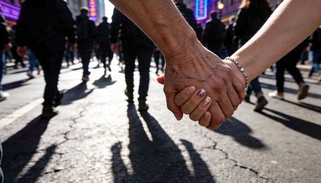 Holding hands across generations on backlit urban street with neon signs and crowd