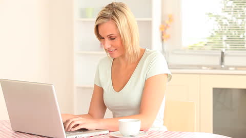 Smiling Woman Using Laptop in Cozy Kitchen Setting