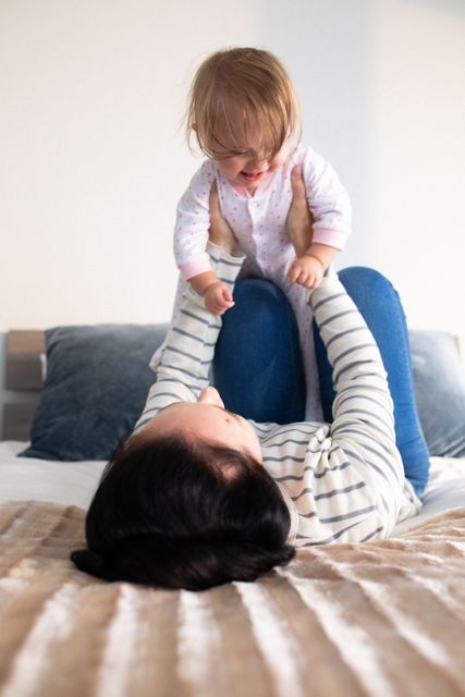 Happy caucasian mother lying on her back on bed lifting smiling baby daughter - Download Free Stock Photos Pikwizard.com