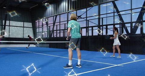Blond player preparing return in indoor paddle tennis doubles on vibrant blue court